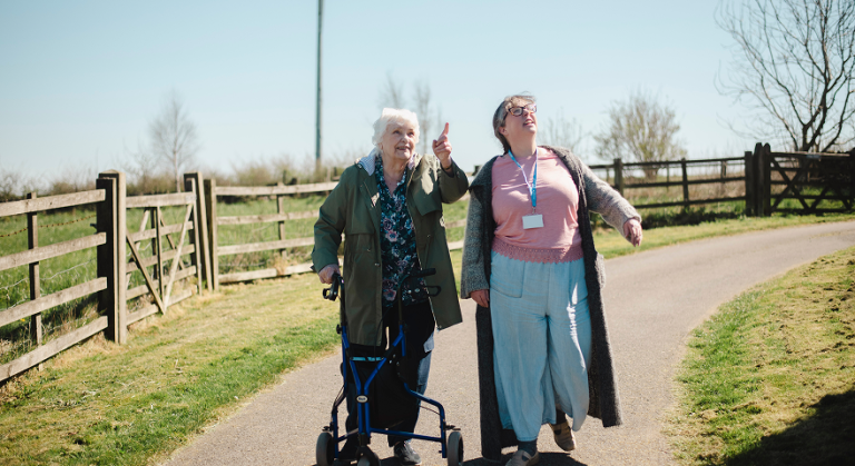 Carer walking outdoors with an elderly woman using a mobility frame