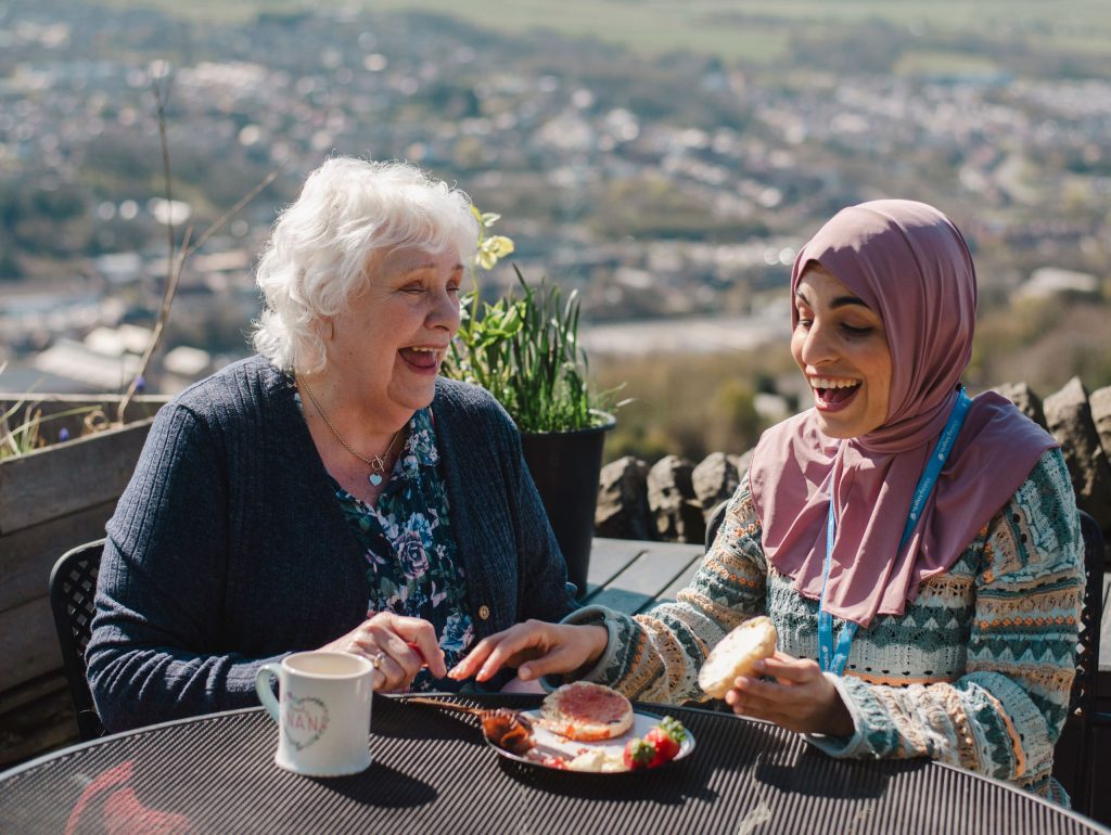 Carer and elderly woman sharing lunch and conversation at home