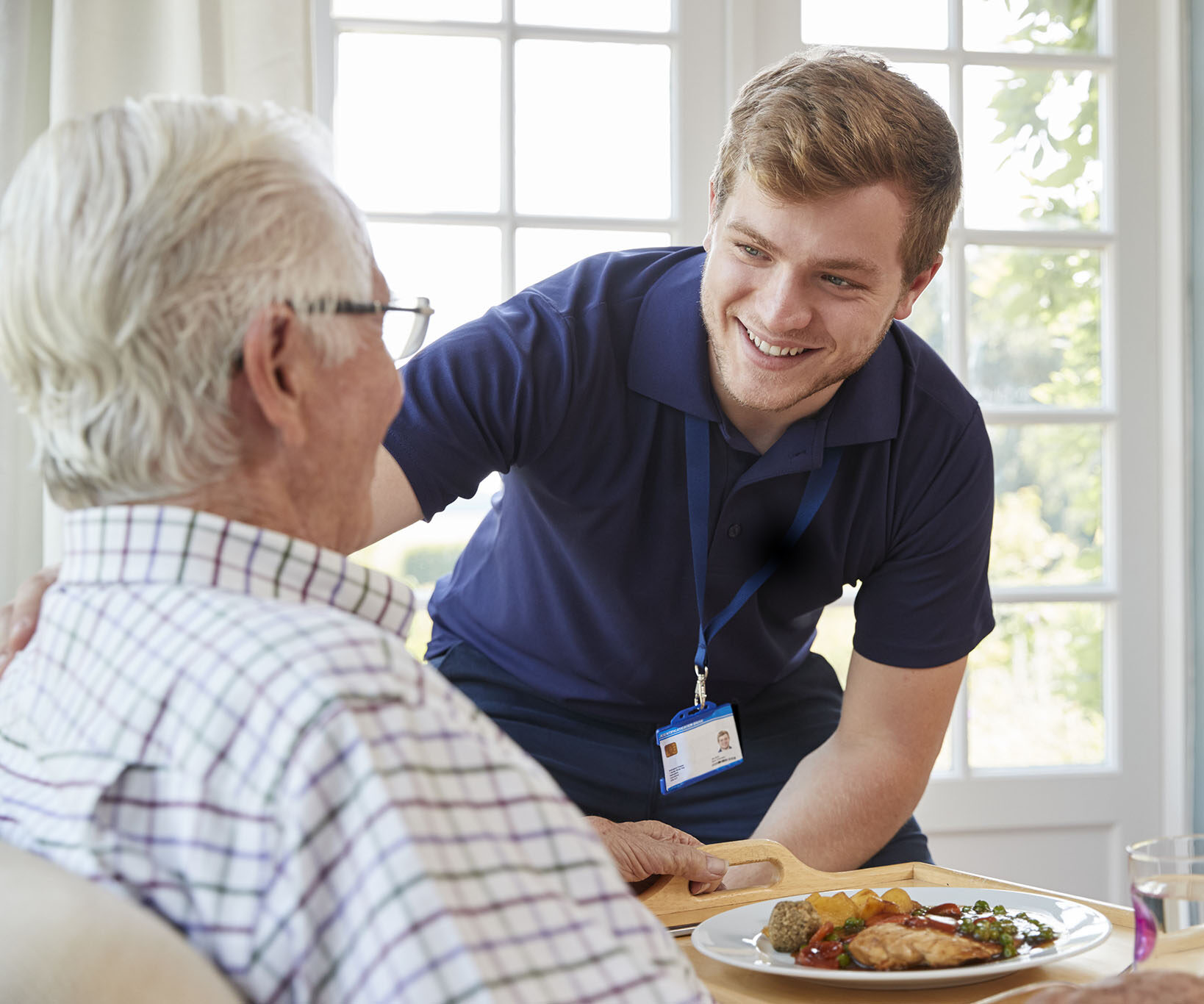 Male care worker serving dinner to a senior man at his home