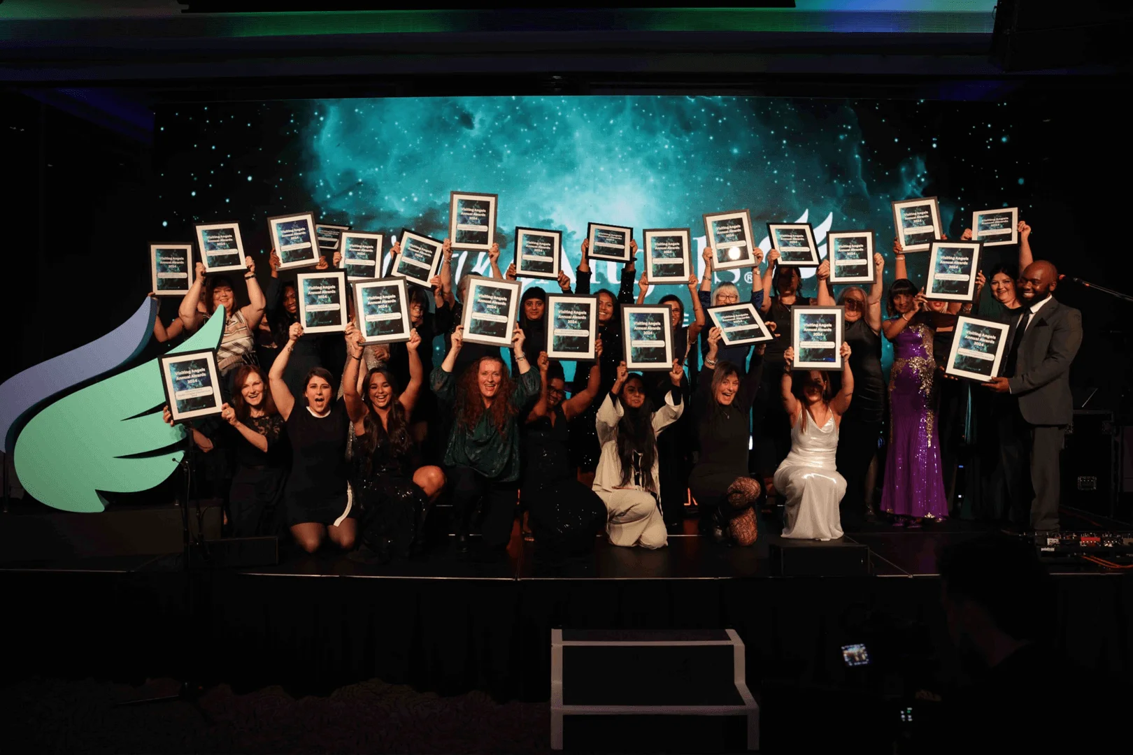 A group of Visiting Angels carers and team members proudly celebrating a Workplace Wellbeing Award on stage in Oxford, Oxfordshire — compassionate, professional, CQC rated home care