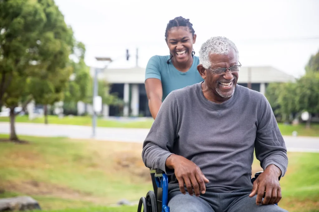A Visiting Angels carer providing personal care support to an elderly man in a wheelchair outdoors in Wheatley, Oxfordshire — compassionate, professional, CQC Good rated home care