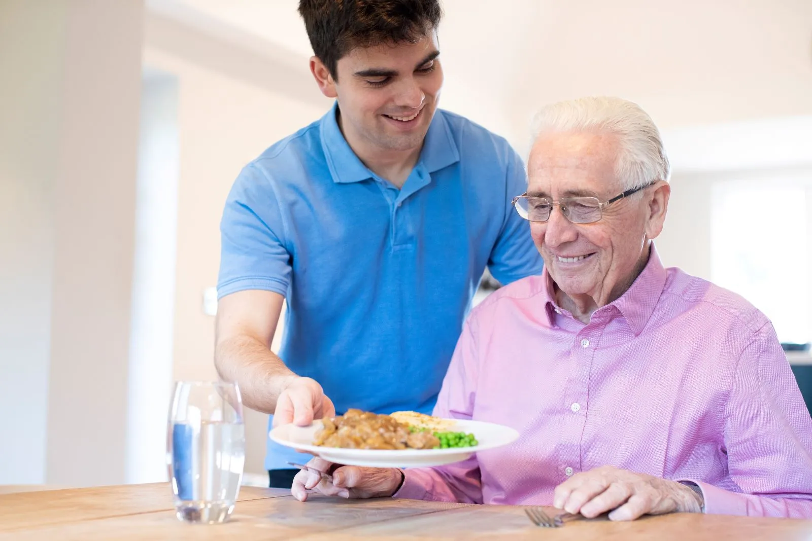 A Visiting Angels carer providing meal assistance and companionship care to an elderly man at home in Oxford, Oxfordshire — compassionate, professional, CQC rated home care