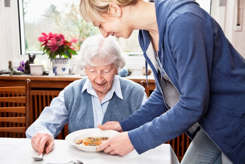 A Visiting Angels carer providing meal assistance to an elderly woman at home in Abingdon, Oxfordshire — compassionate, professional, CQC rated home care