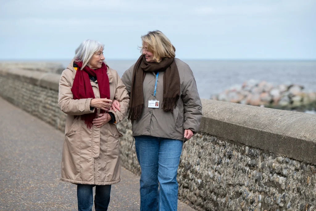 Live-in carer from Visiting Angels Oxford walking with elderly client along a waterfront promenade